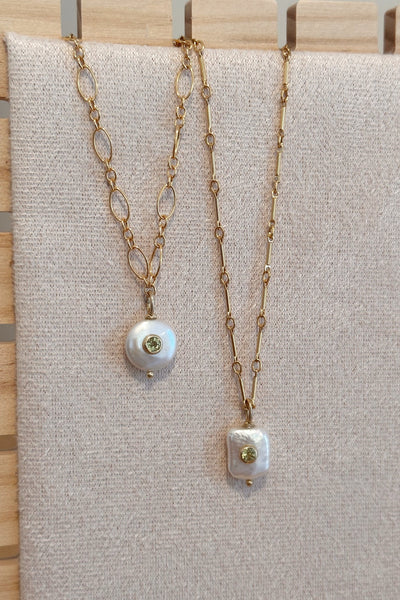 Two gold necklaces with pearl pendants on a beige fabric background