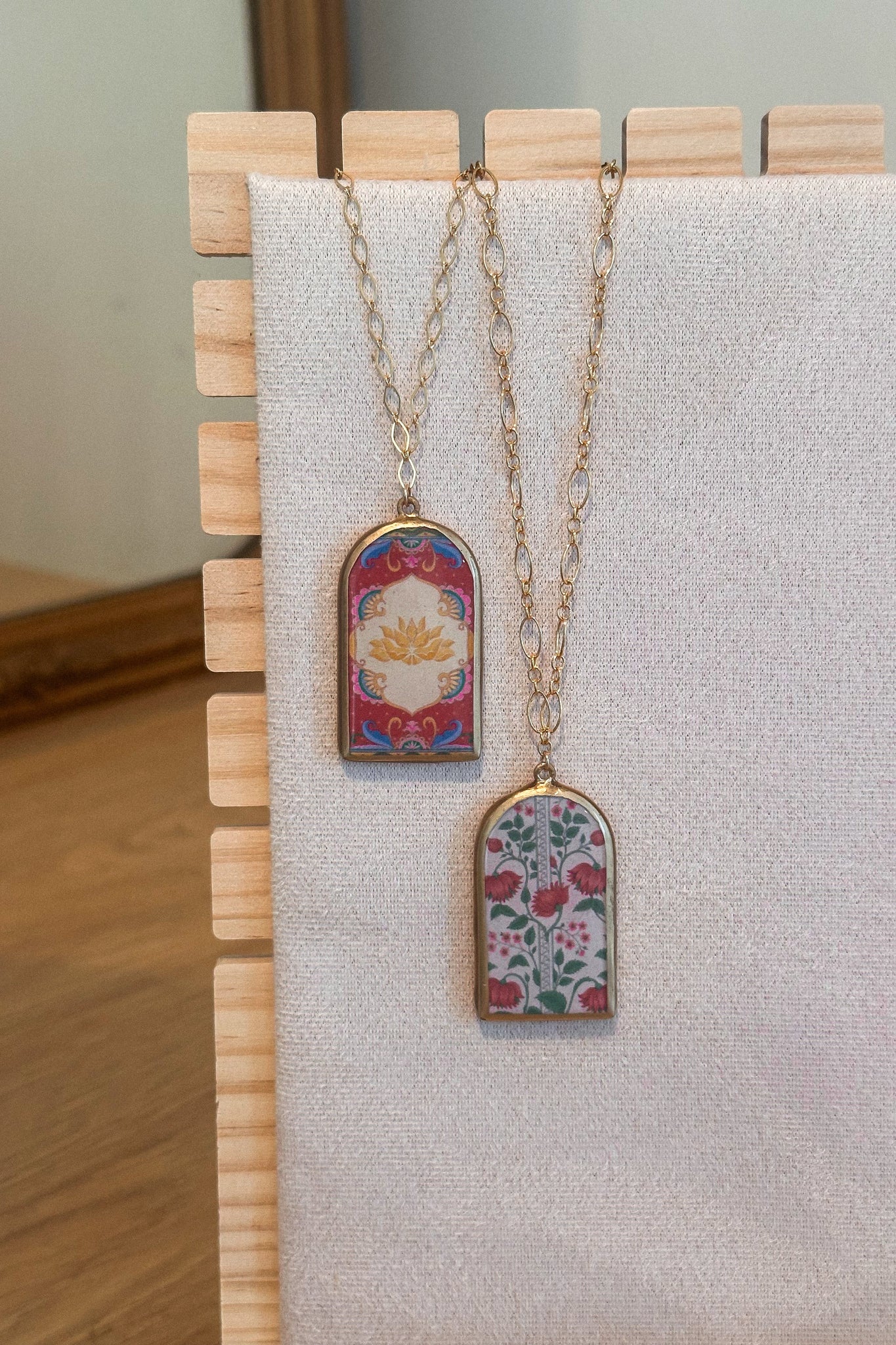 Two necklaces with floral pendants on a wooden stand against a neutral background