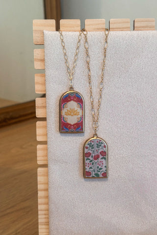 Two necklaces with floral pendants on a wooden stand against a neutral background