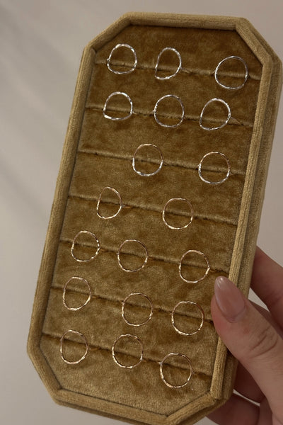 Brown velvet jewelry tray with gold circular rings held by a hand against a neutral background