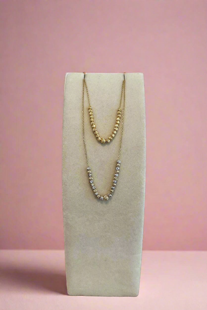 Two necklaces on a white stand with a wooden surface and light gray background