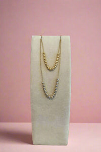 Two necklaces on a white stand with a wooden surface and light gray background