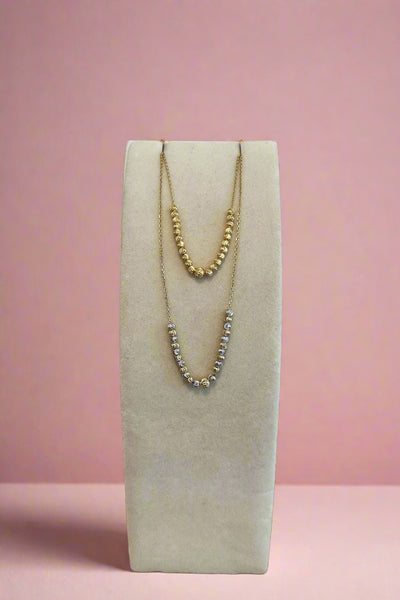 Two necklaces on a white stand with a wooden surface and light gray background