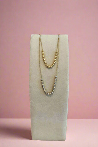 Two necklaces on a white stand with a wooden surface and light gray background
