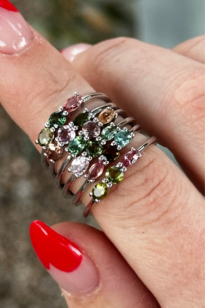 Close-up of a hand wearing multiple gemstone rings with a blurred natural background