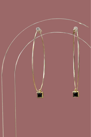 Gold hoop earrings with black square stones on a pink background