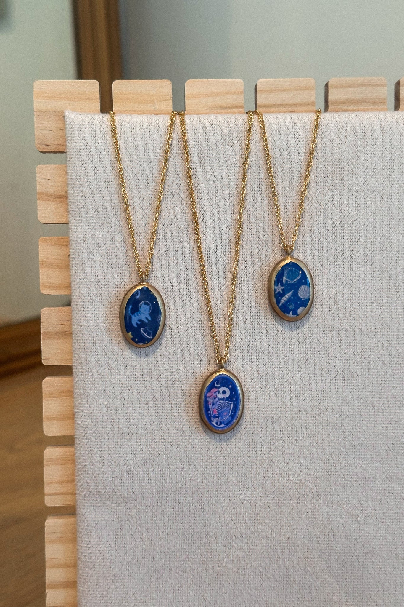 Three necklaces with blue pendant stones on a wooden stand.