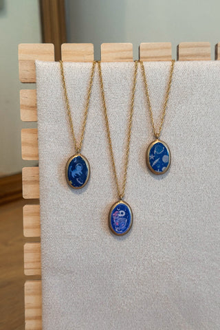 Three necklaces with blue pendant stones on a wooden stand.