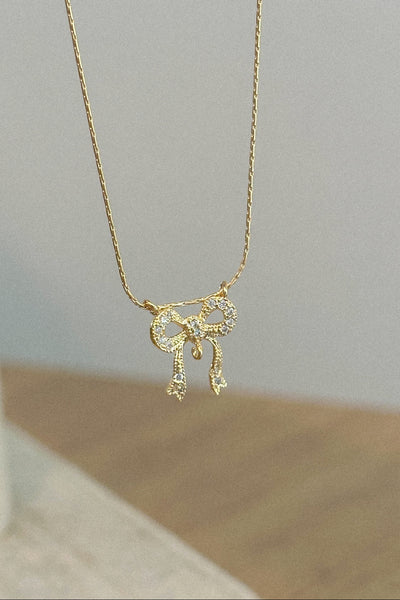 Gold necklace with a bow pendant on a light gray background