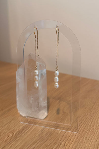 Pair of pearl earrings on a clear stand against a neutral background