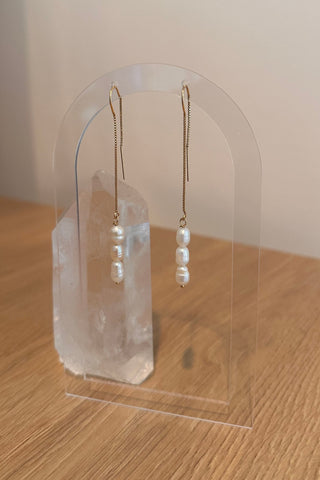 Pair of pearl earrings on a clear stand against a neutral background