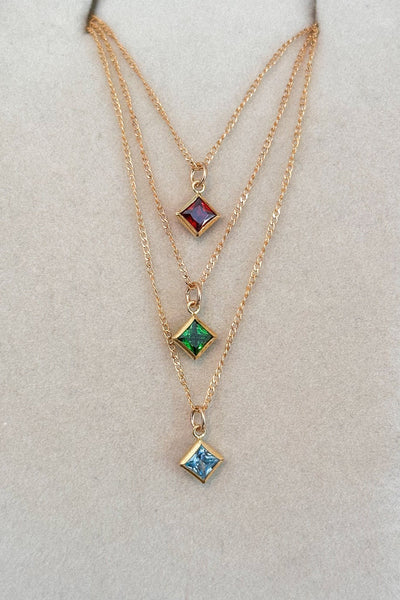 Three gold necklaces with gemstone pendants on a white display stand.