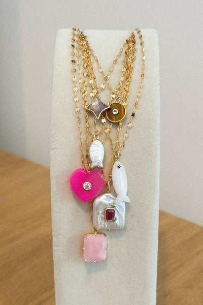 Set of gold necklaces with various pendants on a white stand.