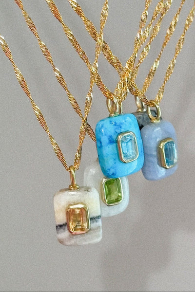 Gold necklaces with various gemstone pendants on a gray background