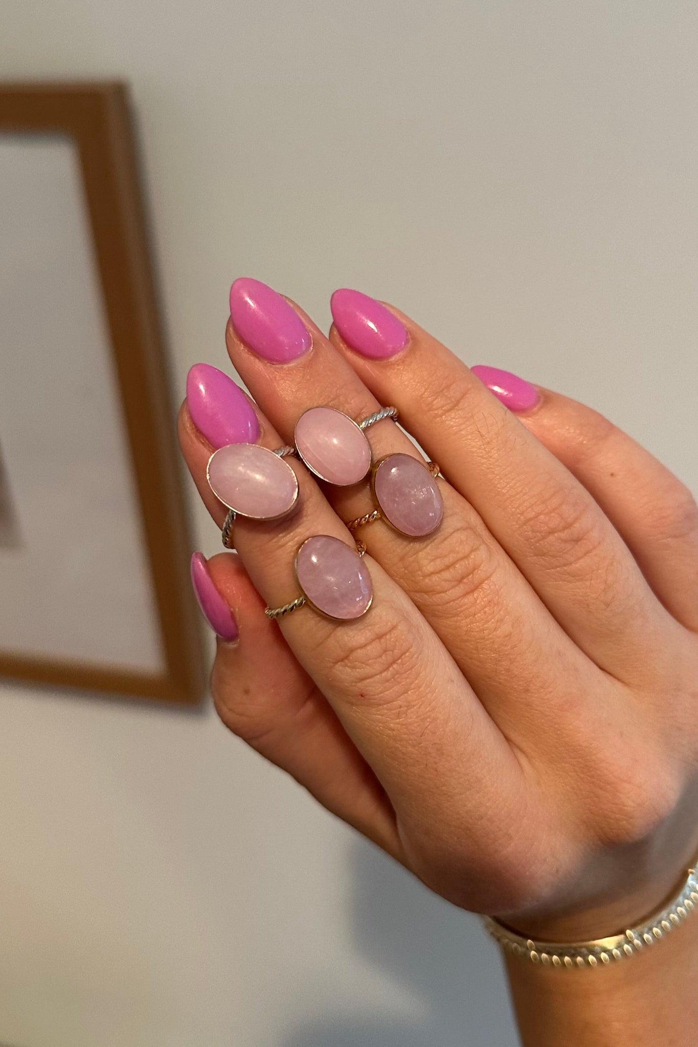 Hand with pink nail polish and rings on a neutral background