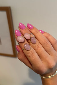 Hand with pink nail polish and rings on a neutral background