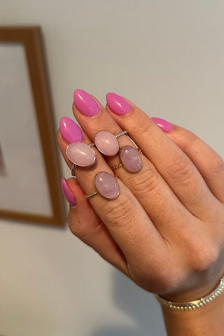 Hand with pink nail polish and rings on a neutral background