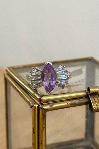 Silver ring with a purple gemstone on a glass display box.