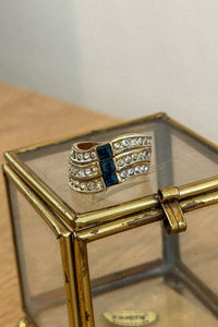 Gold ring with blue gemstone on a glass display stand