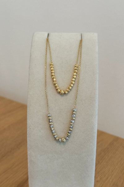 Gold necklace on a white stand with a wooden surface and light gray wall background