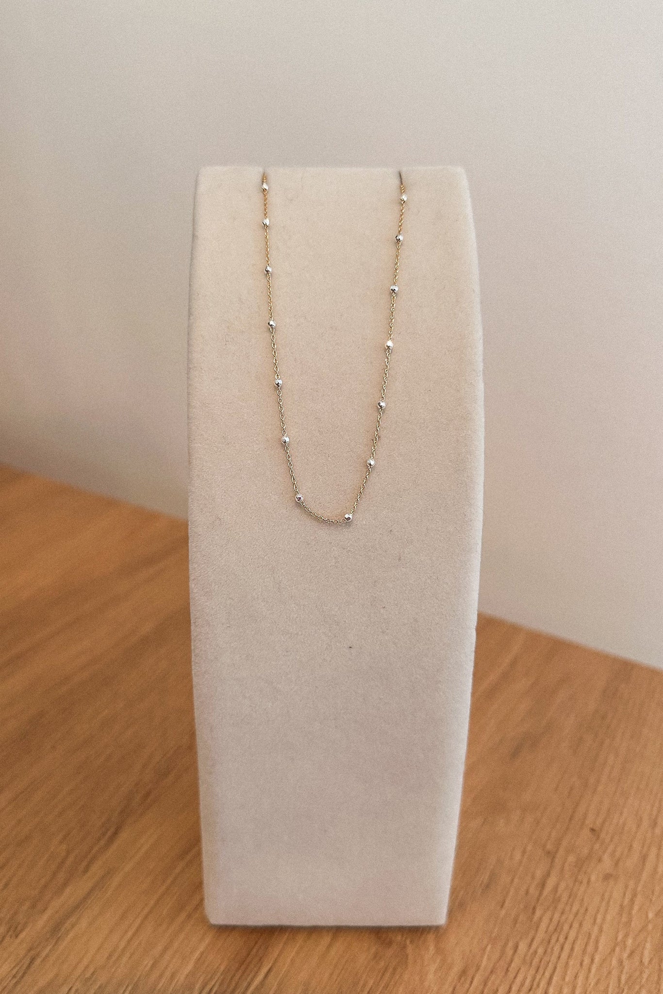 Gold necklace on a white jewelry display stand against a plain background
