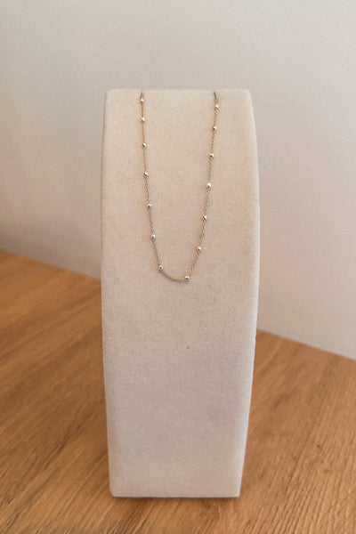 Gold necklace on a white jewelry display stand against a plain background