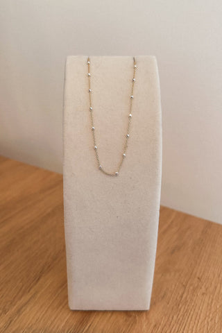 Gold necklace on a white jewelry display stand against a plain background