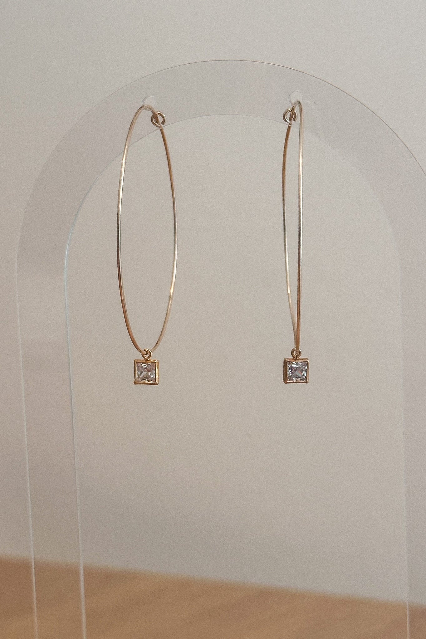 Gold hoop earrings with square gemstones on a clear stand against a white background