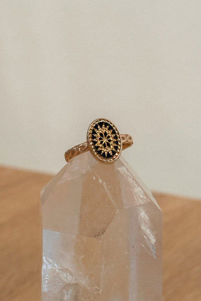 Gold ring with black gemstone on a clear crystal on a wooden surface