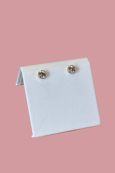 Pair of diamond stud earrings on a white card against a wooden background