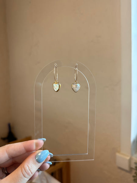 Clear plastic card with heart-shaped earrings held by a hand against a beige background