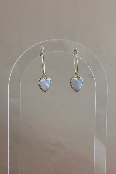Heart-shaped earrings on a clear stand against a neutral background