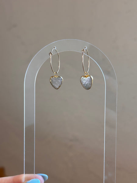 Heart-shaped earrings on a clear stand against a neutral background