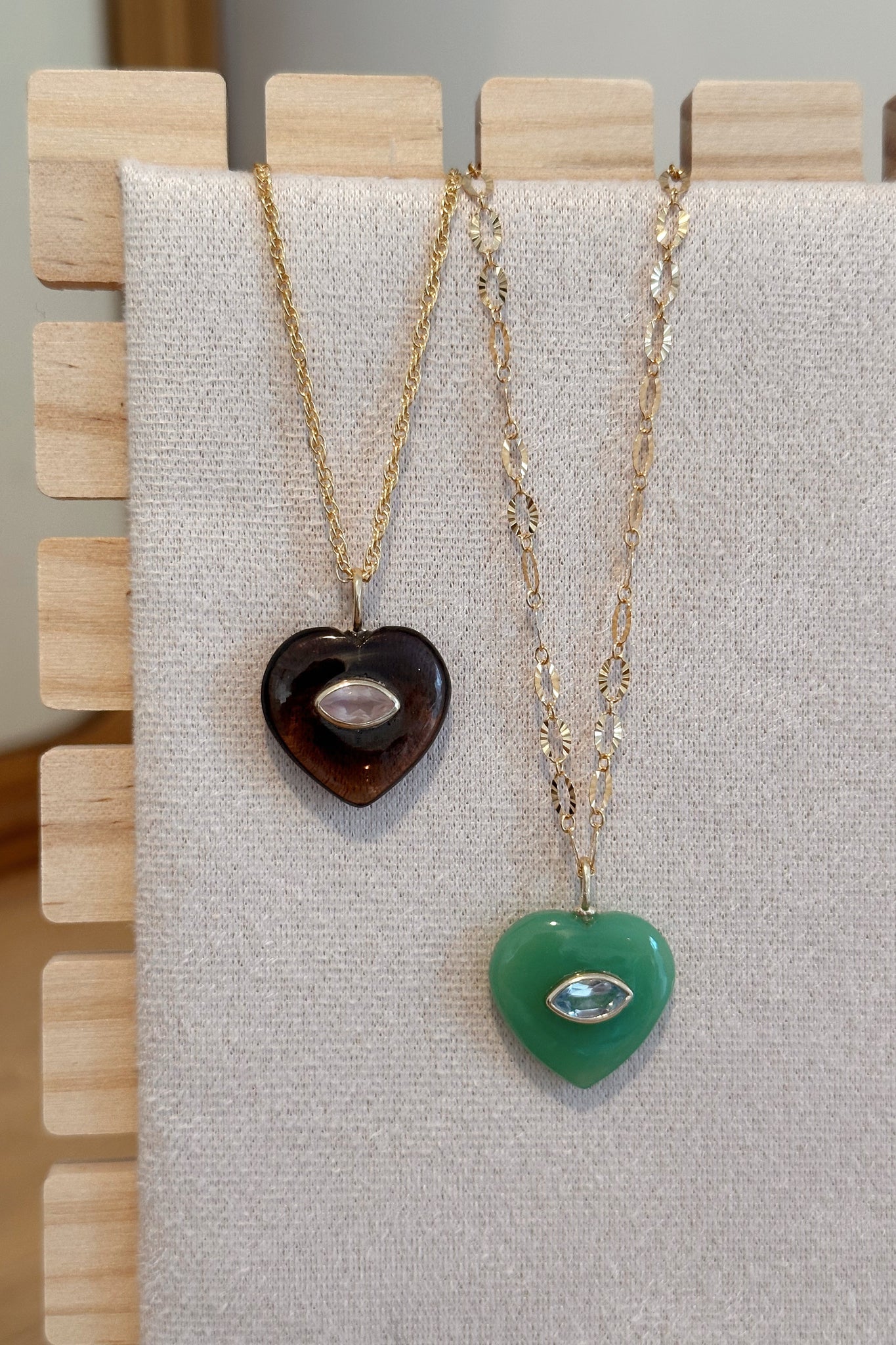 Two heart-shaped pendants on gold necklaces displayed on a gray fabric background.
