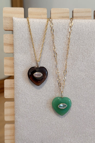 Two heart-shaped pendants on gold necklaces displayed on a gray fabric background.